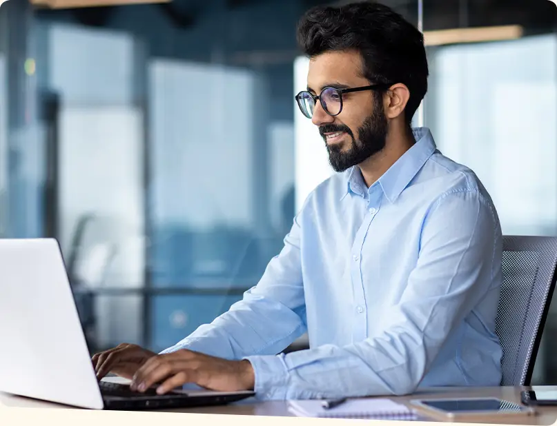 A man smiles as reads something on his laptop.