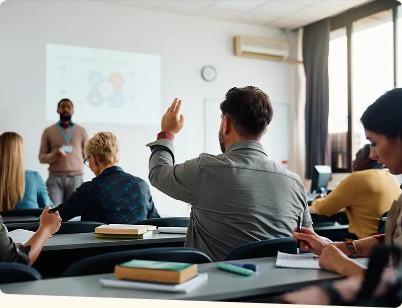 A man raising his hand to answer a question in a classroom.
